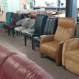 Diverse tweedehands stoelen en fauteuils in verschillende kleuren en stijlen, uitgestald in de winkel