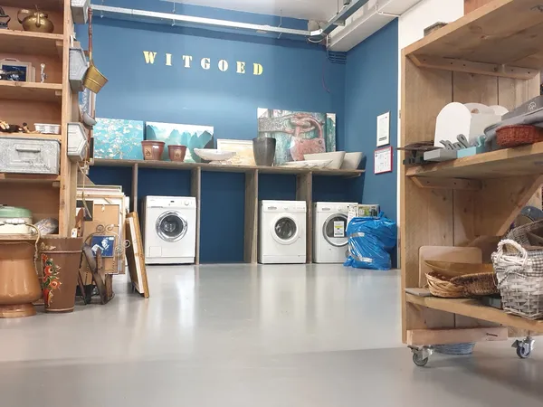 Witgoedafdeling met wasmachines onder houten stellingen en planken met huishoudartikelen