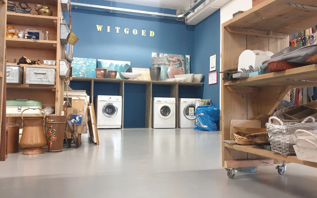 Witgoedafdeling met wasmachines onder houten stellingen en planken met huishoudartikelen