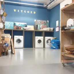 Witgoedafdeling met wasmachines onder houten stellingen en planken met huishoudartikelen
