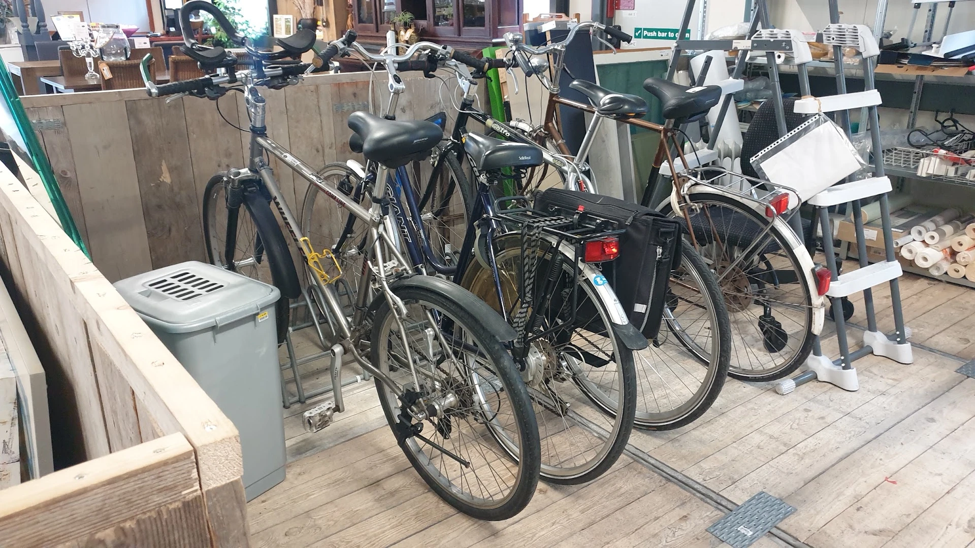 Verschillende tweedehands fietsen uitgestald op een terras buiten de winkel