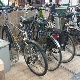Verschillende tweedehands fietsen uitgestald op een terras buiten de winkel