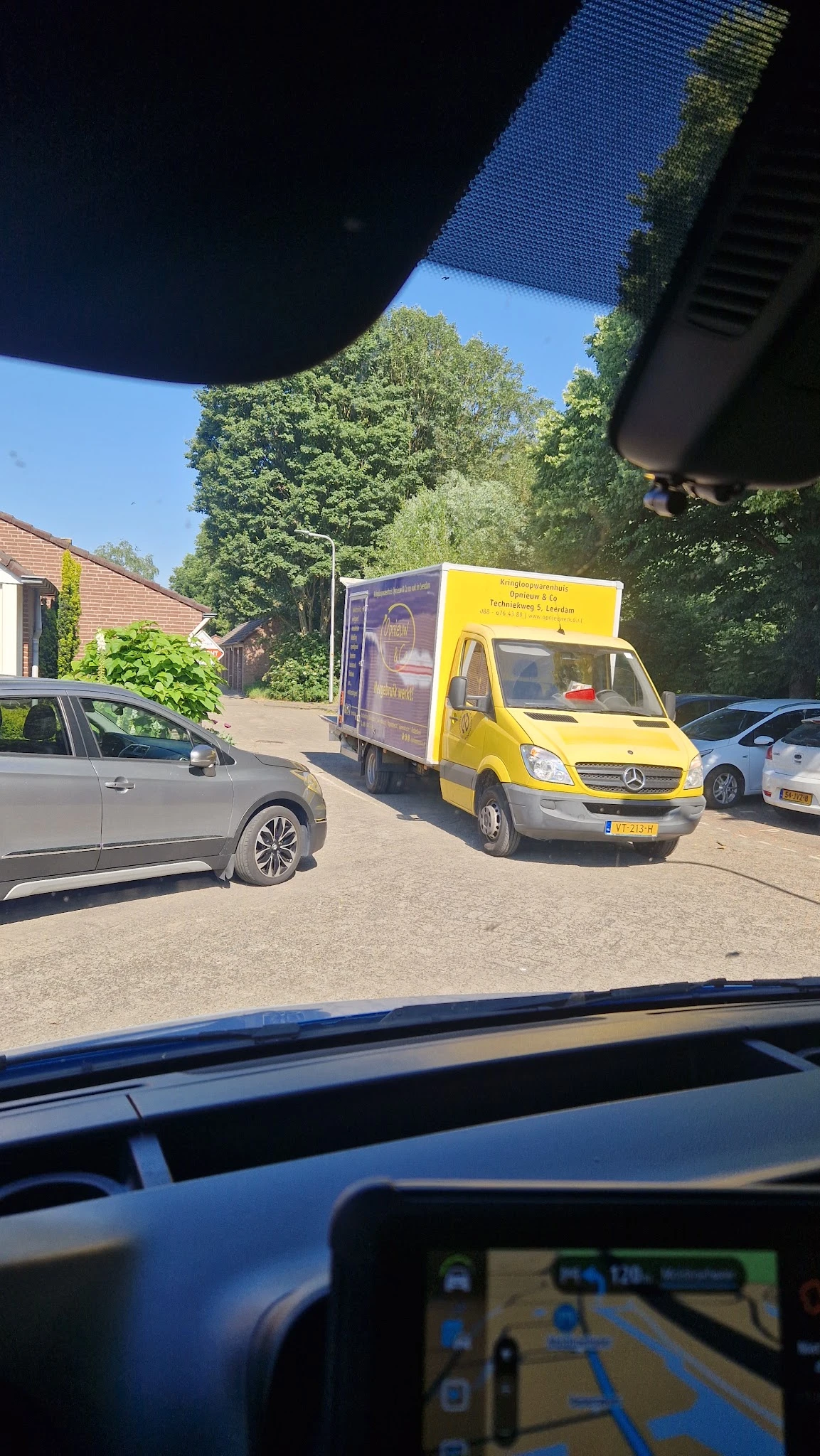 Gele bedrijfsbus met logo van kringloopwinkel geparkeerd op werkterrein tussen andere auto's