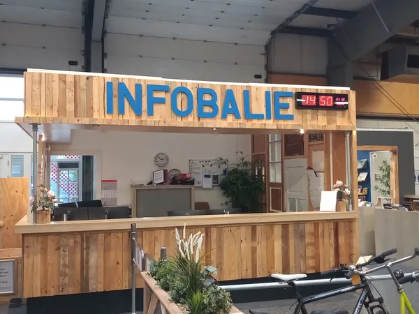 Houten pui van kringloopwinkel met blauwe INFOBALIE-letters en glazen uitstalkast, fiets ervoor