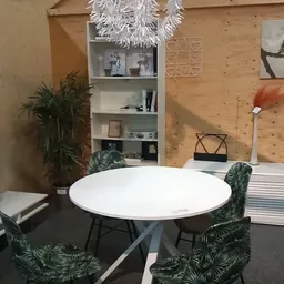 Winkelinterieur met ronde witte tafel, groene stoelen, witte stellingkast, planten en houten muren