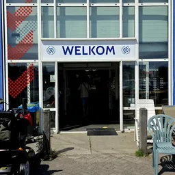 Winkelpui van kringloopwinkel met WELKOM-tekst boven de ingang, glazen deuren en ramen