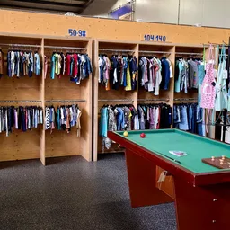Winkelvloer met houten stellingen vol tweedehands kleding en een rode pooltafel