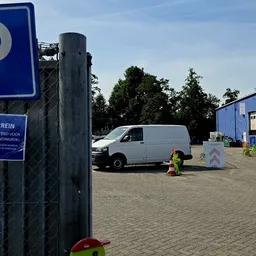 Parkeerplaats met blauwe P-bord, witte bestelwagen en blauwe bedrijfsgebouw op de achtergrond