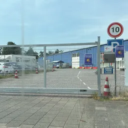 Ingang van kringloopwinkel met gesloten hek, snelheidsbord en bouwmaterialen zichtbaar