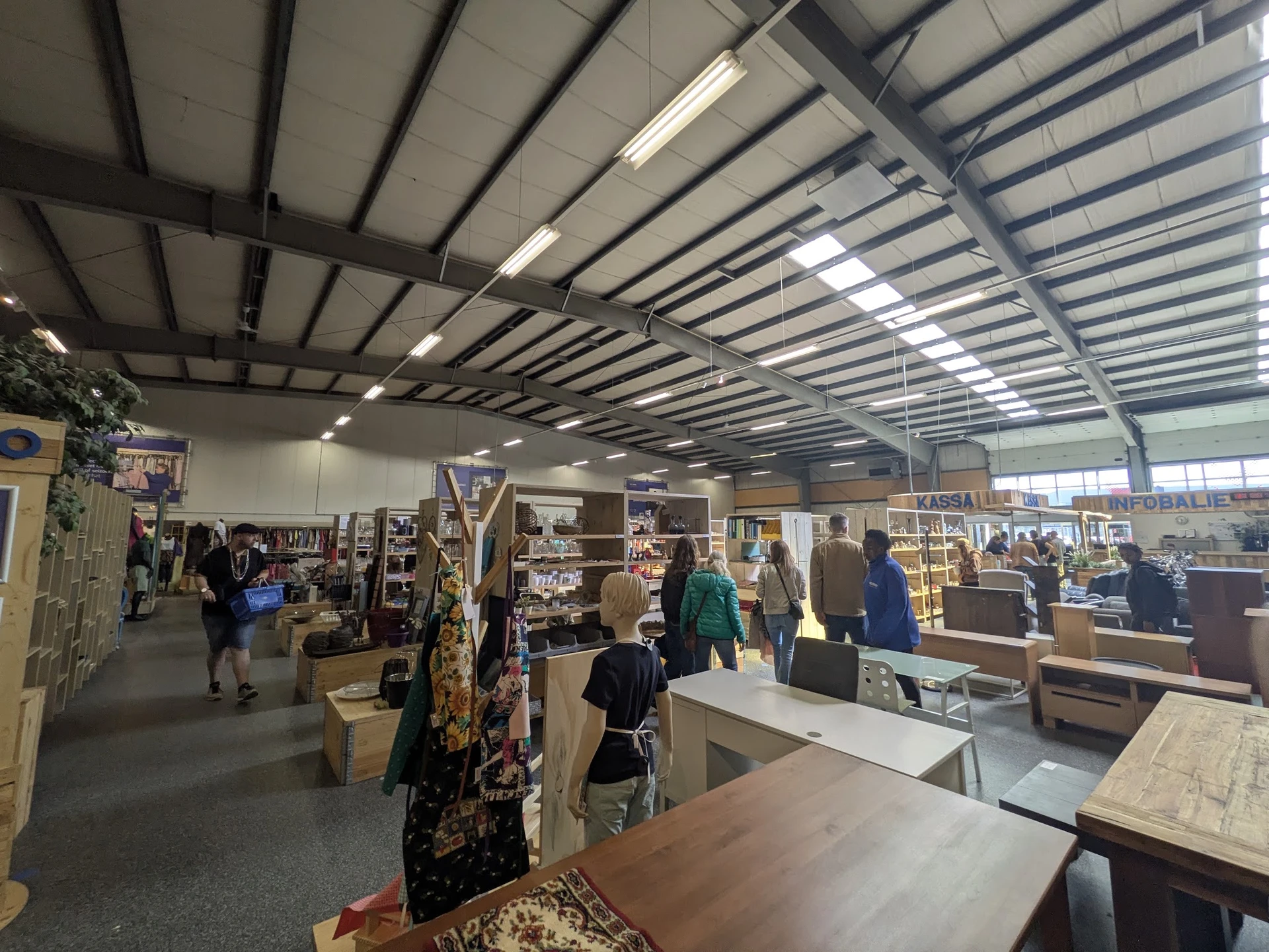 Winkelvloer van kringloopwinkel met stellingen, rekken met spullen en bezoekers die rondlopen