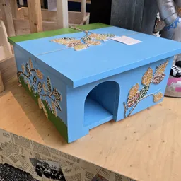 Blauwe houten kattenhuisje met goudkleurige decoratieve details op het dak