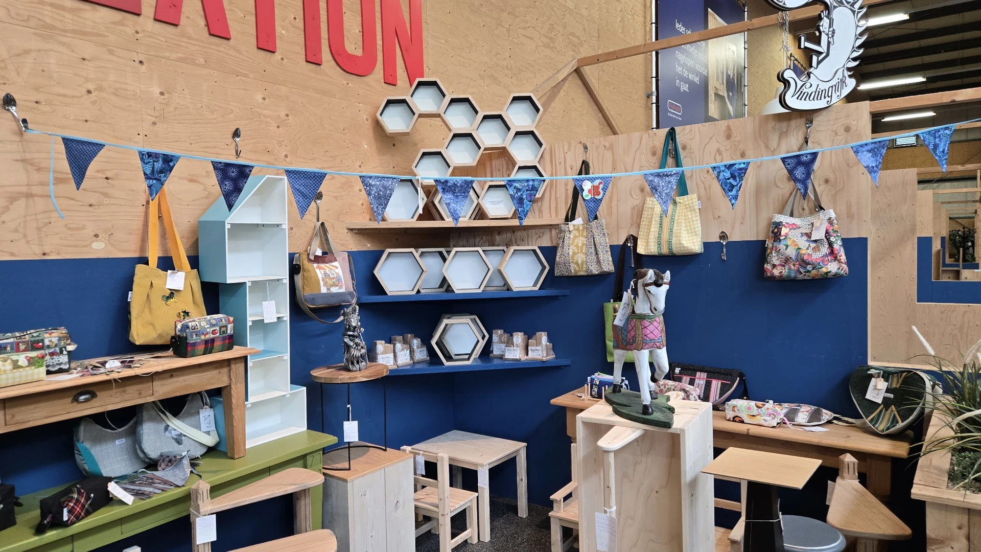 Winkelinterieur met blauwe wand, houten stellingen met hexagonale dozen, bunting-vlaggen, en diverse uitgestalde spullen