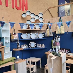 Winkelinterieur met blauwe wand, houten stellingen met hexagonale dozen, bunting-vlaggen, en diverse uitgestalde spullen