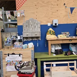 Werkruimte met houten werkbank, blauwe muur, gereedschap, muziekinstrumenten en diverse spullen op planken