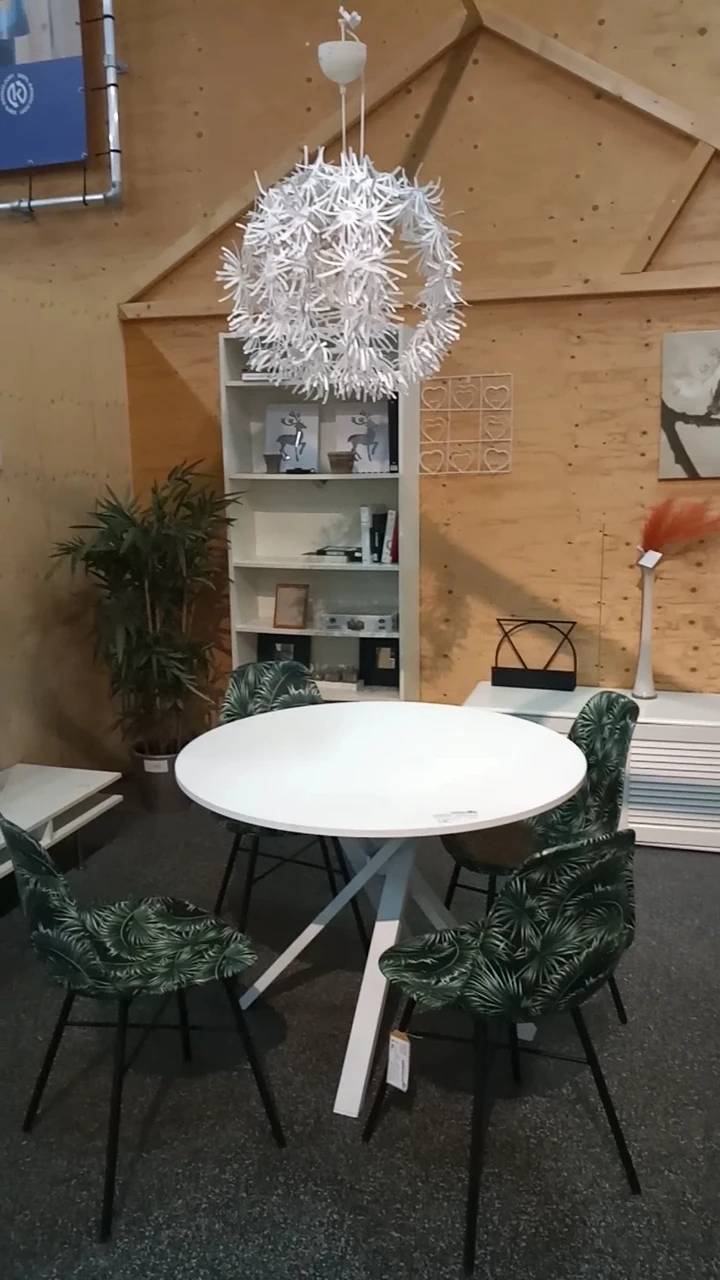 Winkelinterieur met rond wit tafelblad, groene stoelen, planken met decoratie en houten wand