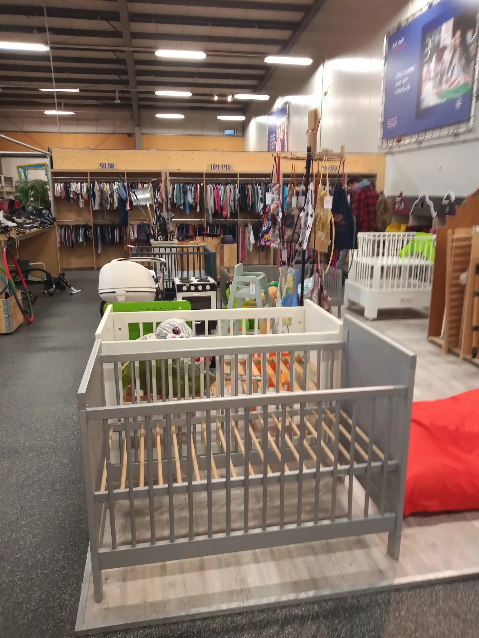 Babywiegjes en kindermeubels uitgestald in de winkel met kledingrekken op de achtergrond