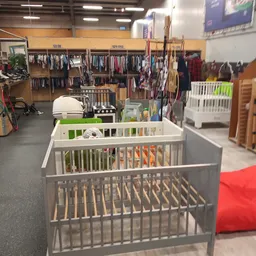 Babywiegjes en kindermeubels uitgestald in de winkel met kledingrekken op de achtergrond