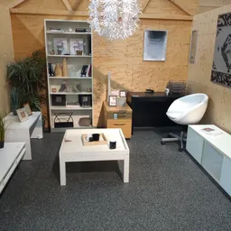 Winkelvloer met uitgestalde meubels en decoratieartikelen, waaronder een witte salontafel, zwarte piano, wit stoeltje en open