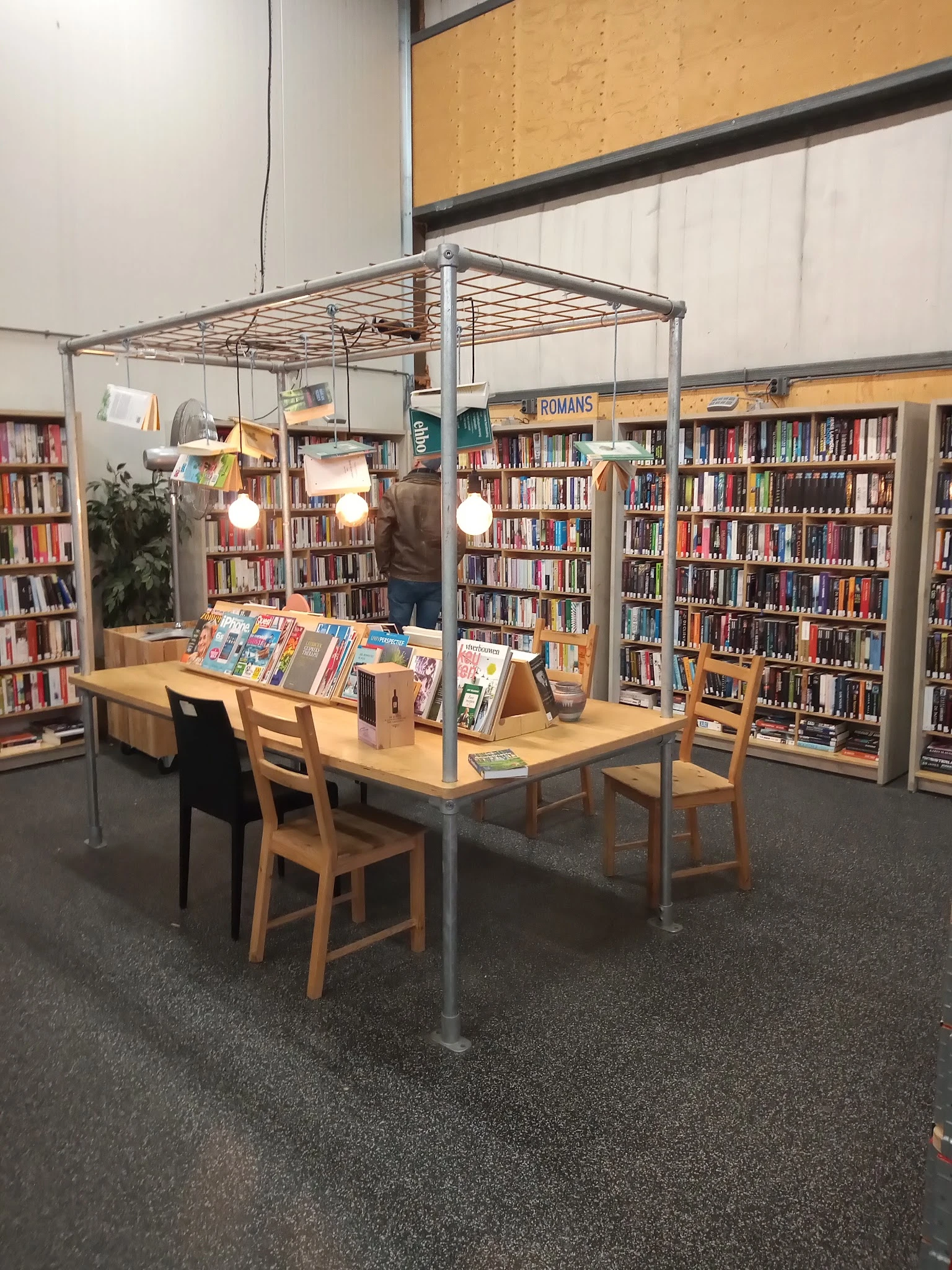Boekenrek met tafel en stoelen in een bibliotheekruimte met boekenkasten op de achtergrond