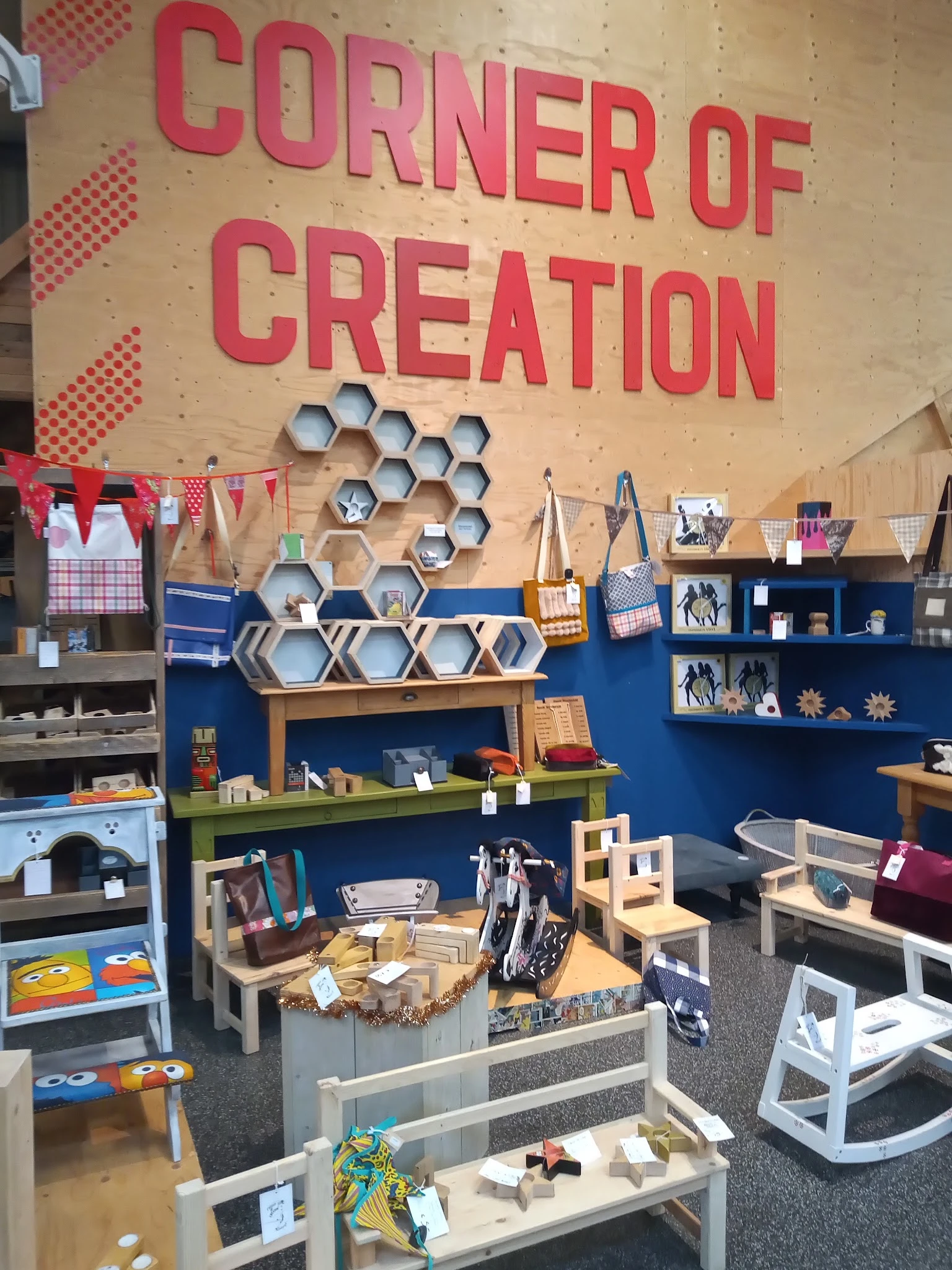 Winkelinterieur met blauwe wanden, houten hexagon wandplanken, groene plank, houten stoeltjes en diverse artikelen op stellin