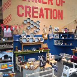 Winkelinterieur met blauwe wanden, houten hexagon wandplanken, groene plank, houten stoeltjes en diverse artikelen op stellin