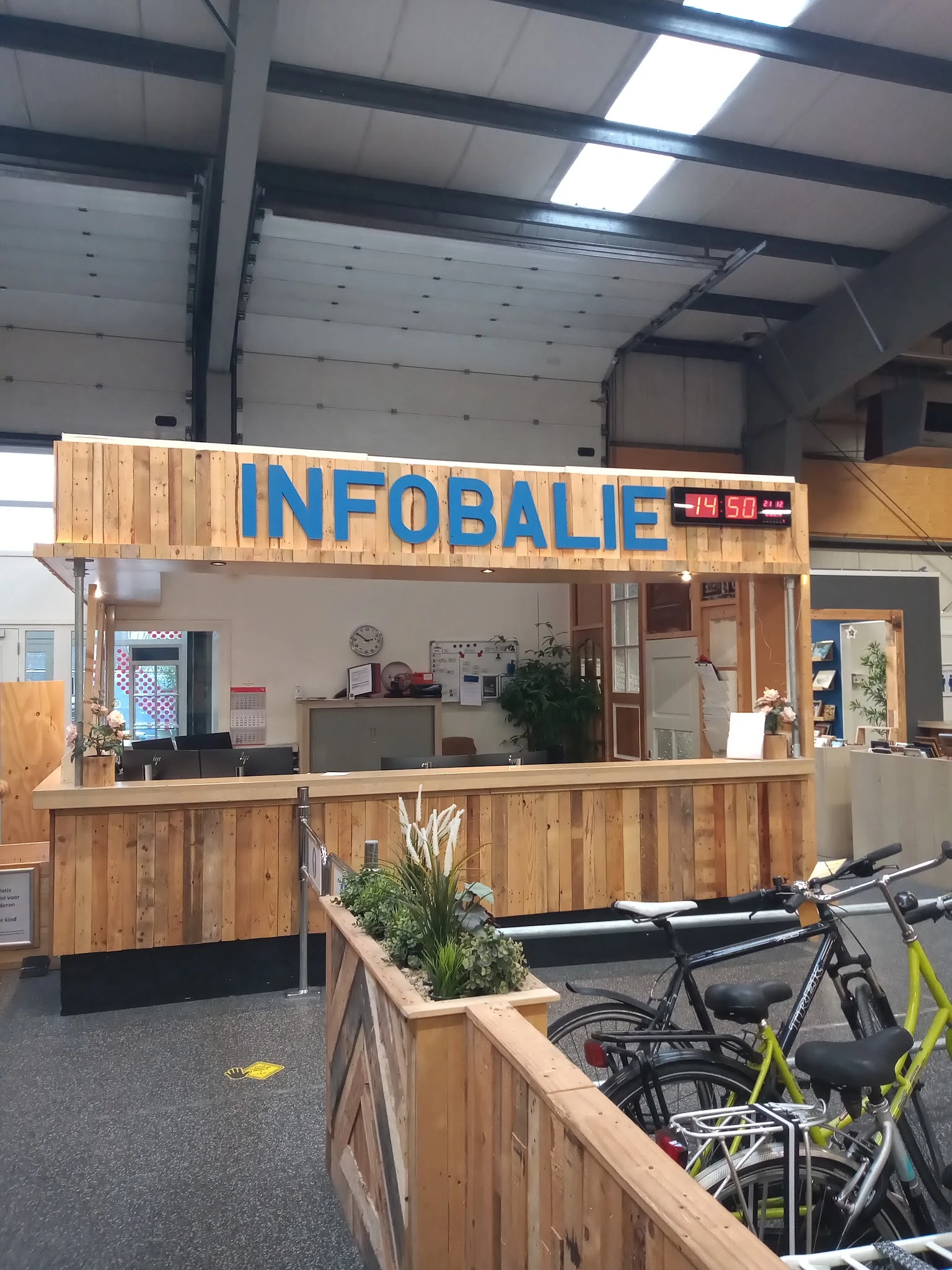 Houten gevel van kringloopwinkel met blauwe INFOBALIE-letters en ingang