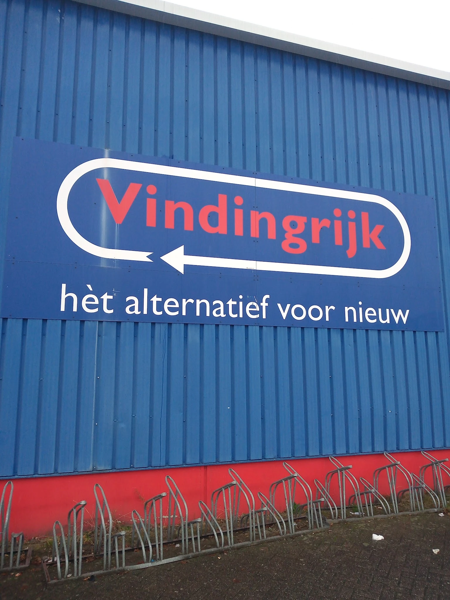 Blauwe gevel met wit en rood logo en pijl van kringloopwinkel Vindingrijk met tagline