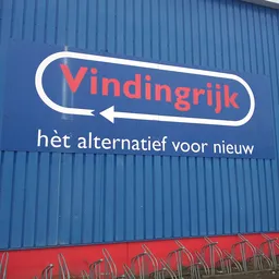 Blauwe gevel met wit en rood logo en pijl van kringloopwinkel Vindingrijk met tagline