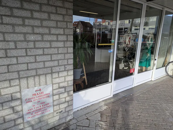 Voorgevel van kringloopwinkel met glazen deuren en ramen, brickwork zijwand, opgeplakt informatiebord links