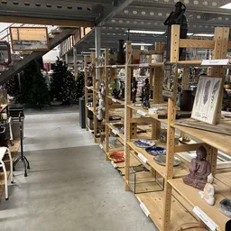 Winkelvloer met houten stellingen vol decoratieve artikelen, beeldjes en serviesgoed in een kringloopwinkel