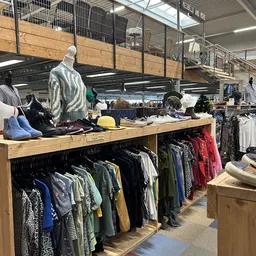 Houten display met tweedehands kleding, waaronder jassen en truien op hangers, met een mannequin bovenop