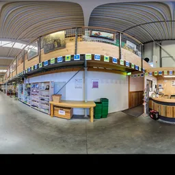 Ruim interieur van kringloopwinkel met houten plafond, stellingen, informatieborden en balie aan rechterkant
