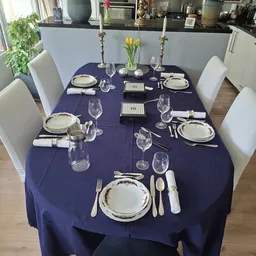 Gedekte tafel met servies, glazen en bestek voor zes personen op donkerblauwe tafelkleed