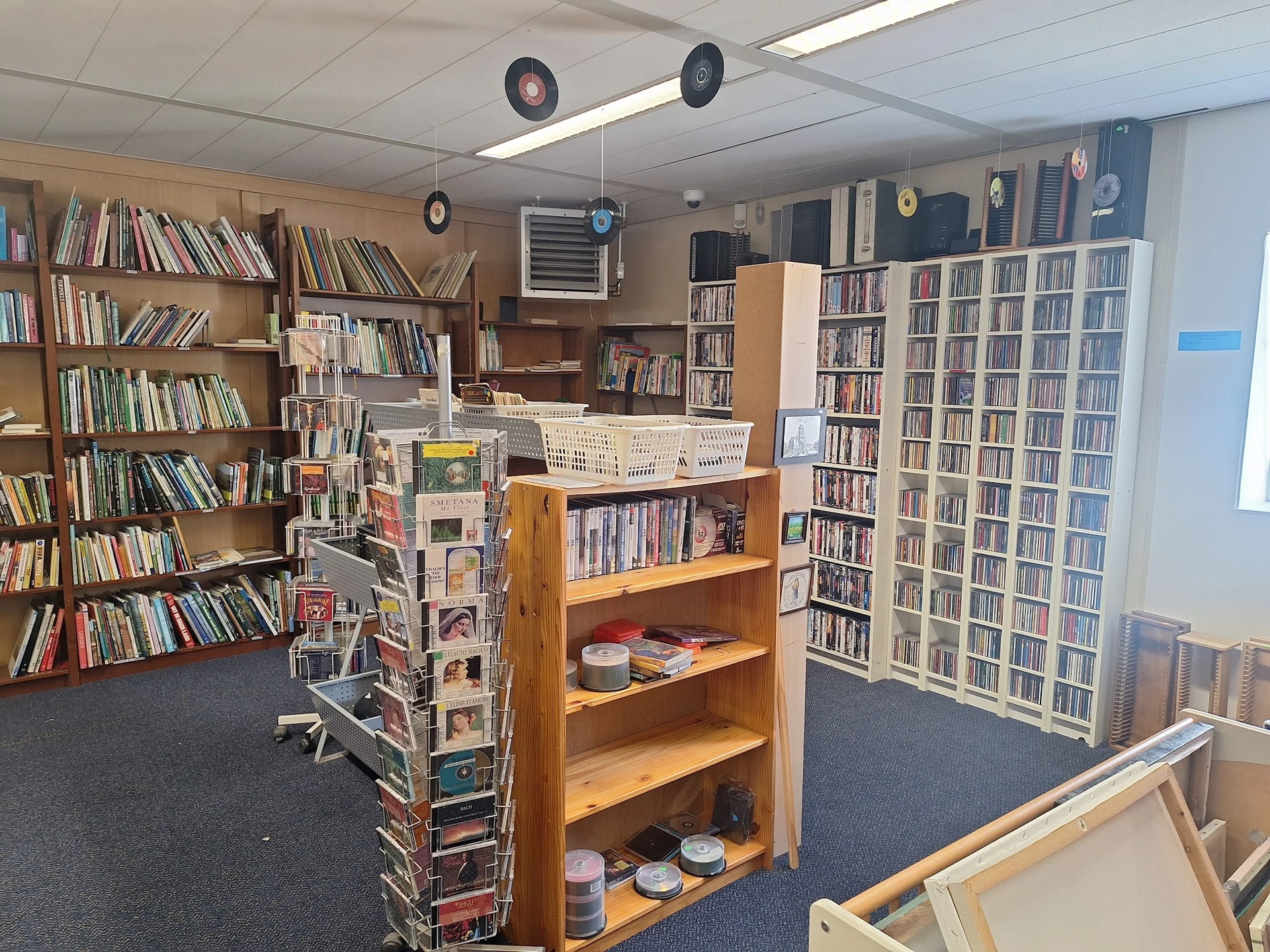 Binnenaanzicht van kringloopwinkel met houten boekenkasten, stellingen vol boeken en diverse tweedehands spullen op planken