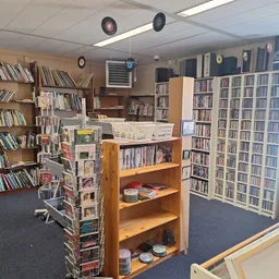 Binnenaanzicht van kringloopwinkel met houten boekenkasten, stellingen vol boeken en diverse tweedehands spullen op planken