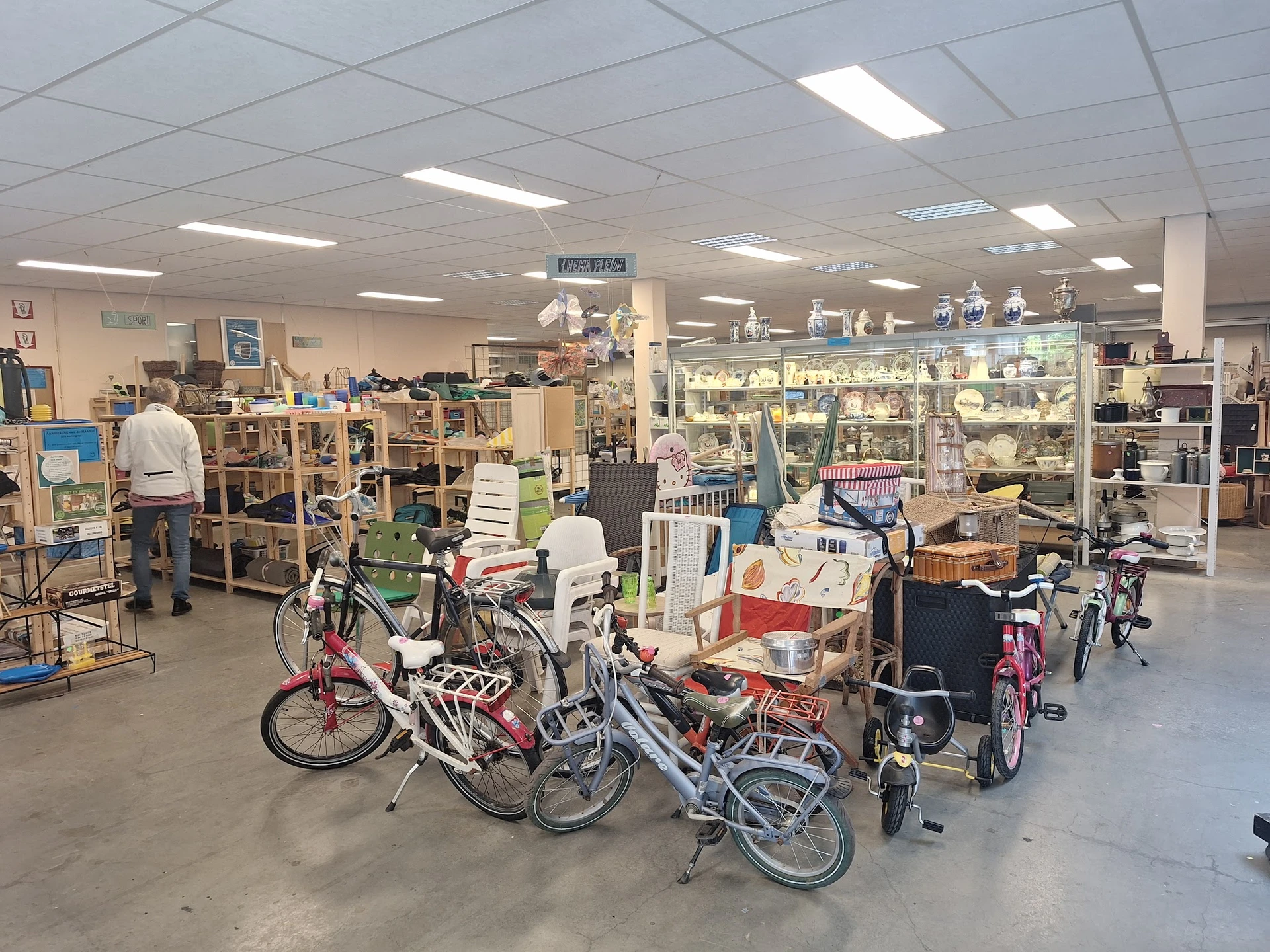 Winkelvloer met diverse fietsen en tweedehandsartikelen, stellingen vol spullen op achtergrond