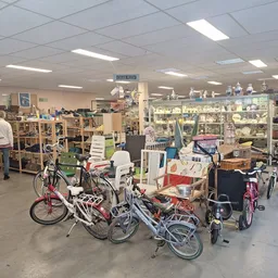 Winkelvloer met diverse fietsen en tweedehandsartikelen, stellingen vol spullen op achtergrond
