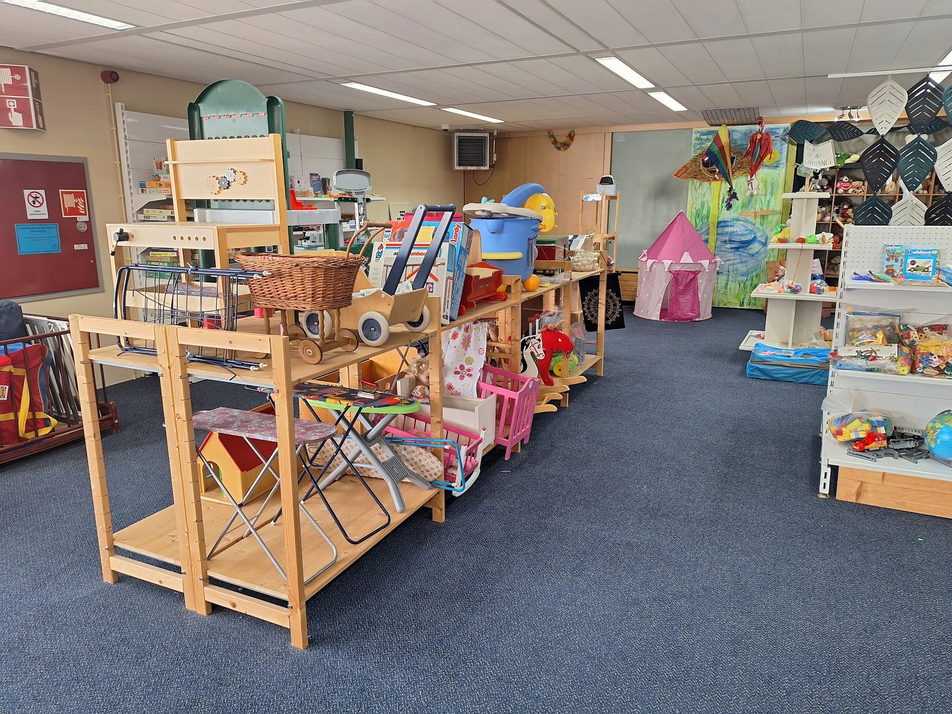 Speelgoedafdeling in kringloopwinkel met houten stellingen, speelhuisjes, gitaren en ander kinderpeelgoed op blauwe vloer