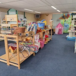 Speelgoedafdeling in kringloopwinkel met houten stellingen, speelhuisjes, gitaren en ander kinderpeelgoed op blauwe vloer
