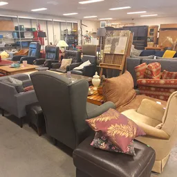 Winkelvloer met diverse zitmeubels: grijze stoelen, beige fauteuils, rode pluche bank en andere tweedehands meubelstukken uit