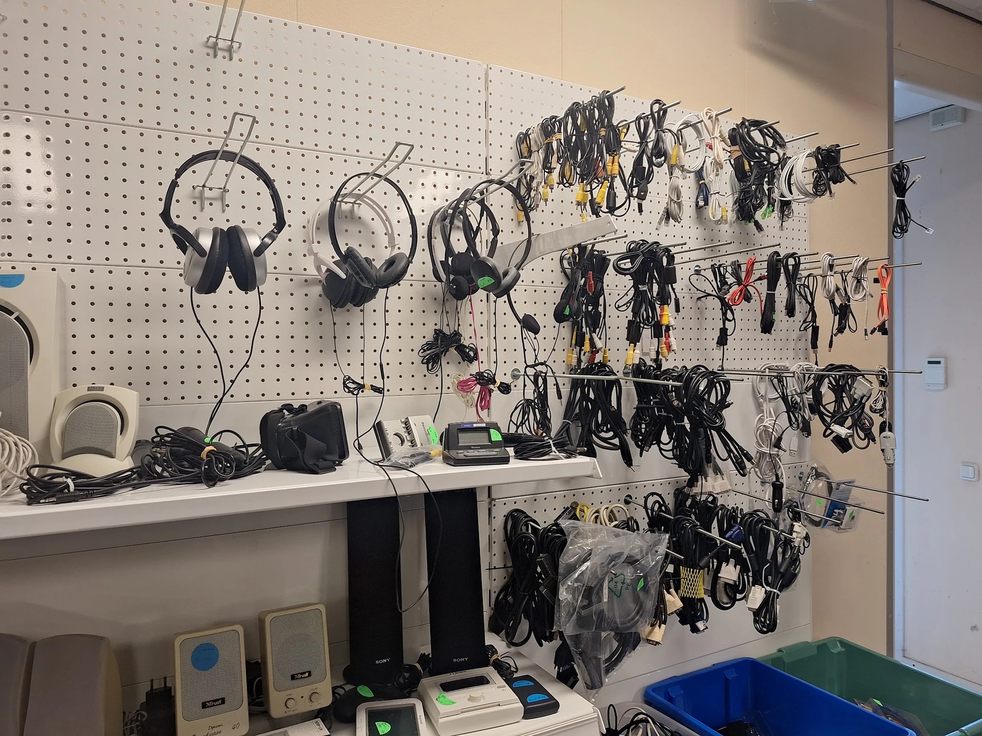 Pegbord met uitgestalde elektronica en kabels, waaronder koptelefoons, audioapparatuur en accessoires