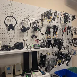 Pegbord met uitgestalde elektronica en kabels, waaronder koptelefoons, audioapparatuur en accessoires