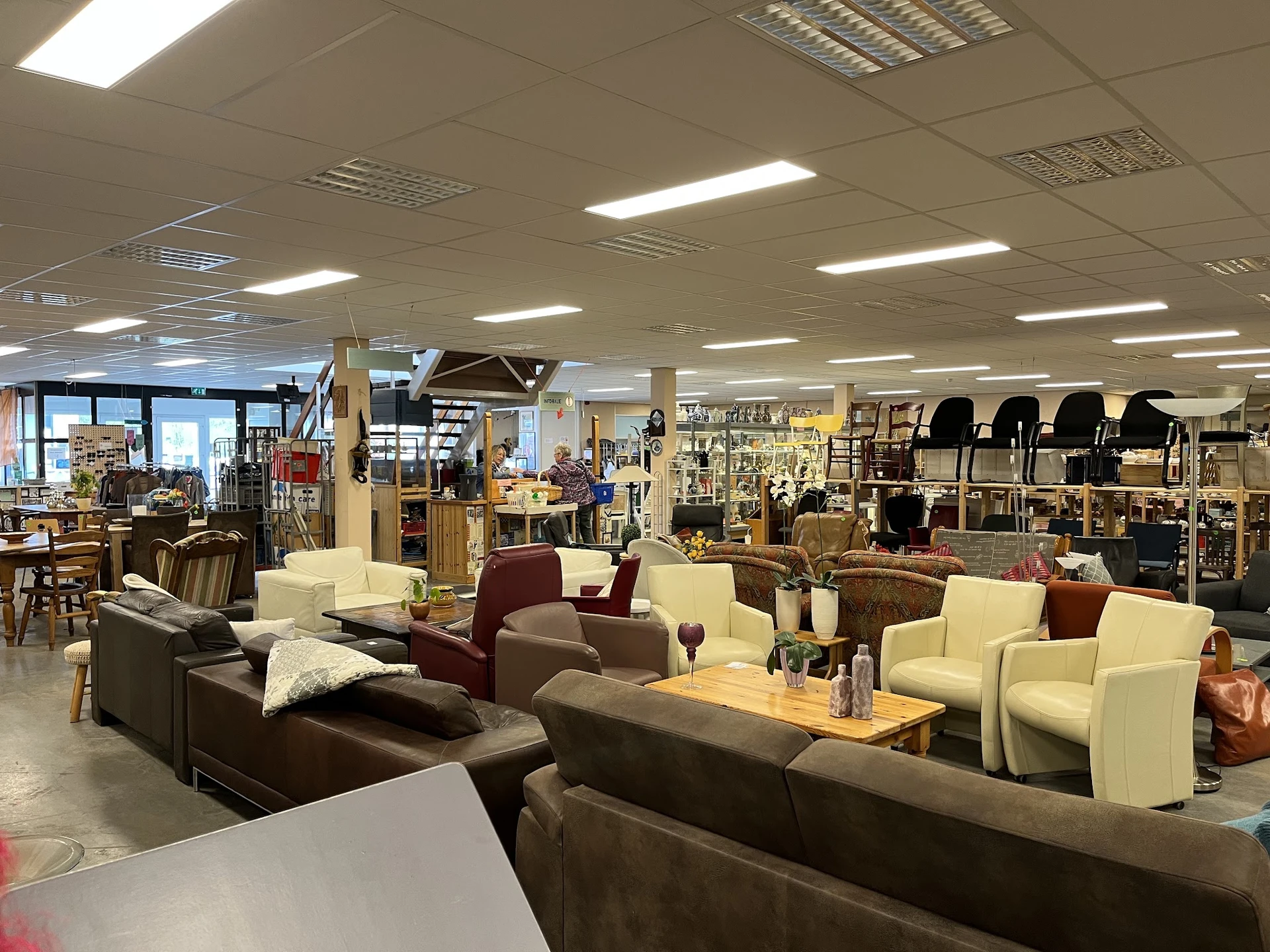 Winkelvloer met diverse meubels: bruine en beige zitmeubels, tafels en stoelen in een kringloopwinkel