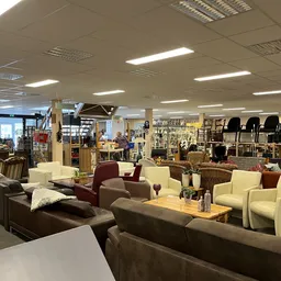 Winkelvloer met diverse meubels: bruine en beige zitmeubels, tafels en stoelen in een kringloopwinkel