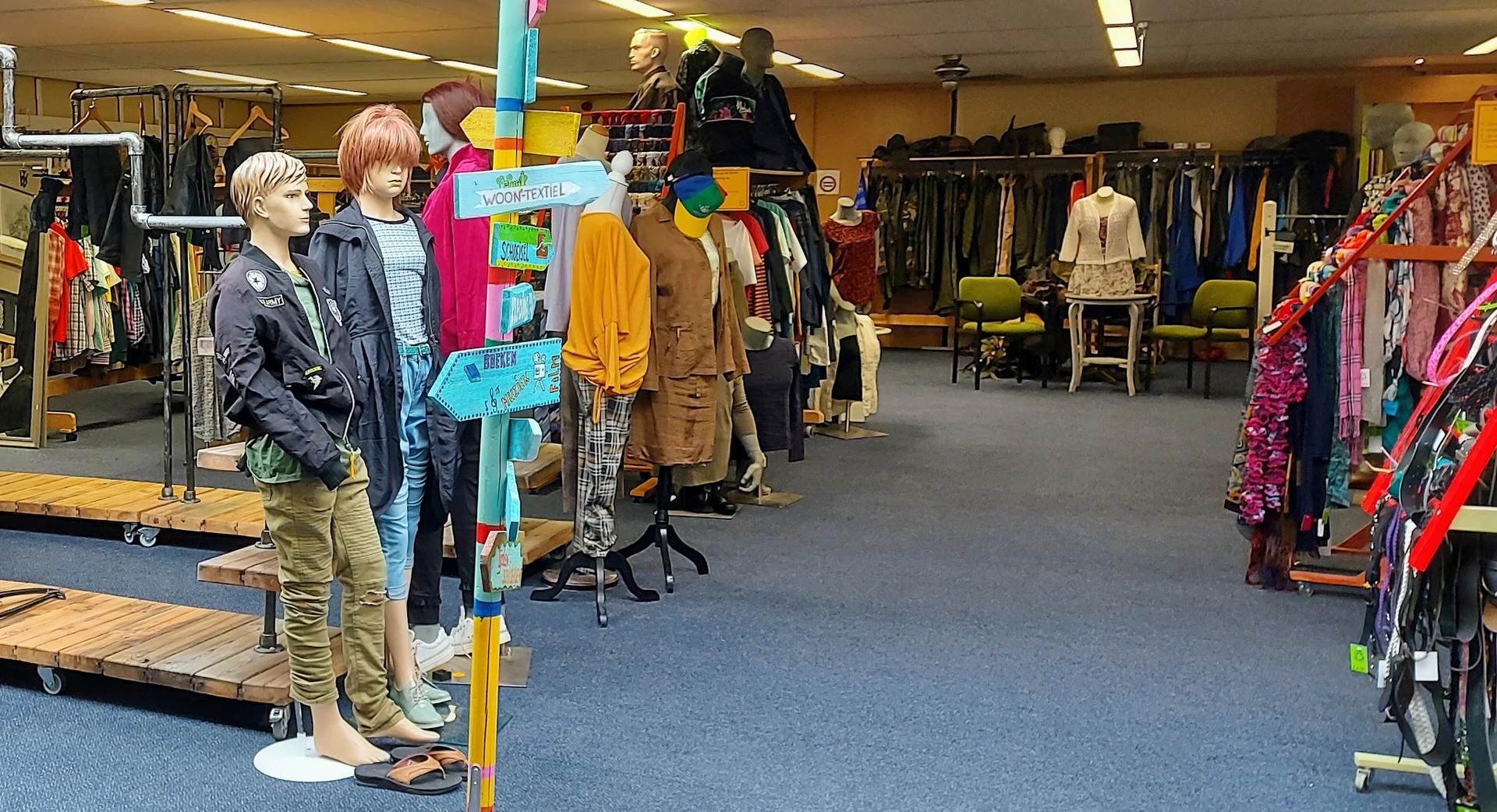 Binnenzicht van kringloopwinkel met kledingrekken, etalagepoppen en bezoekers die kleding bekijken