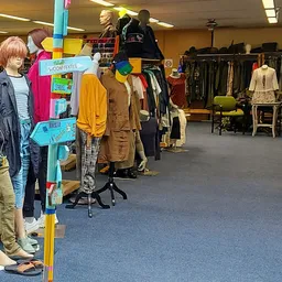 Binnenzicht van kringloopwinkel met kledingrekken, etalagepoppen en bezoekers die kleding bekijken