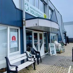 Moderne gevel van kringloopwinkel met glazen deuren, blauwe en witte bekleding, terras met stoelen en openlucht uitstalling