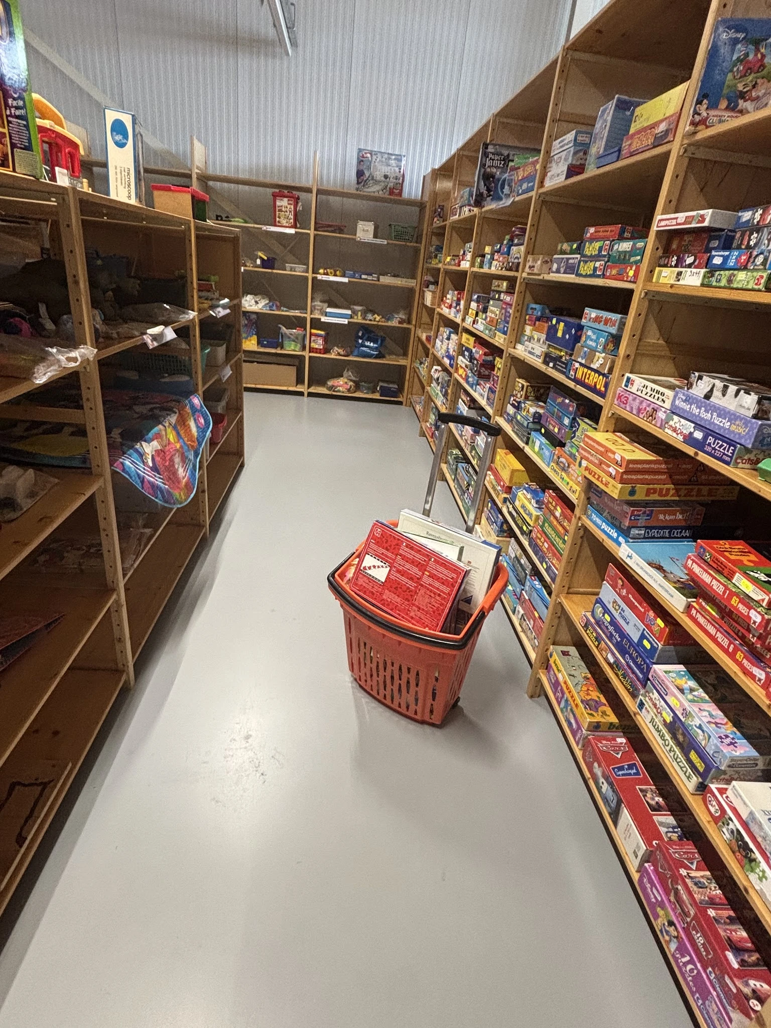 Winkelvloer met winkelmandje tussen boekenrekken vol dvd's en bordspellen