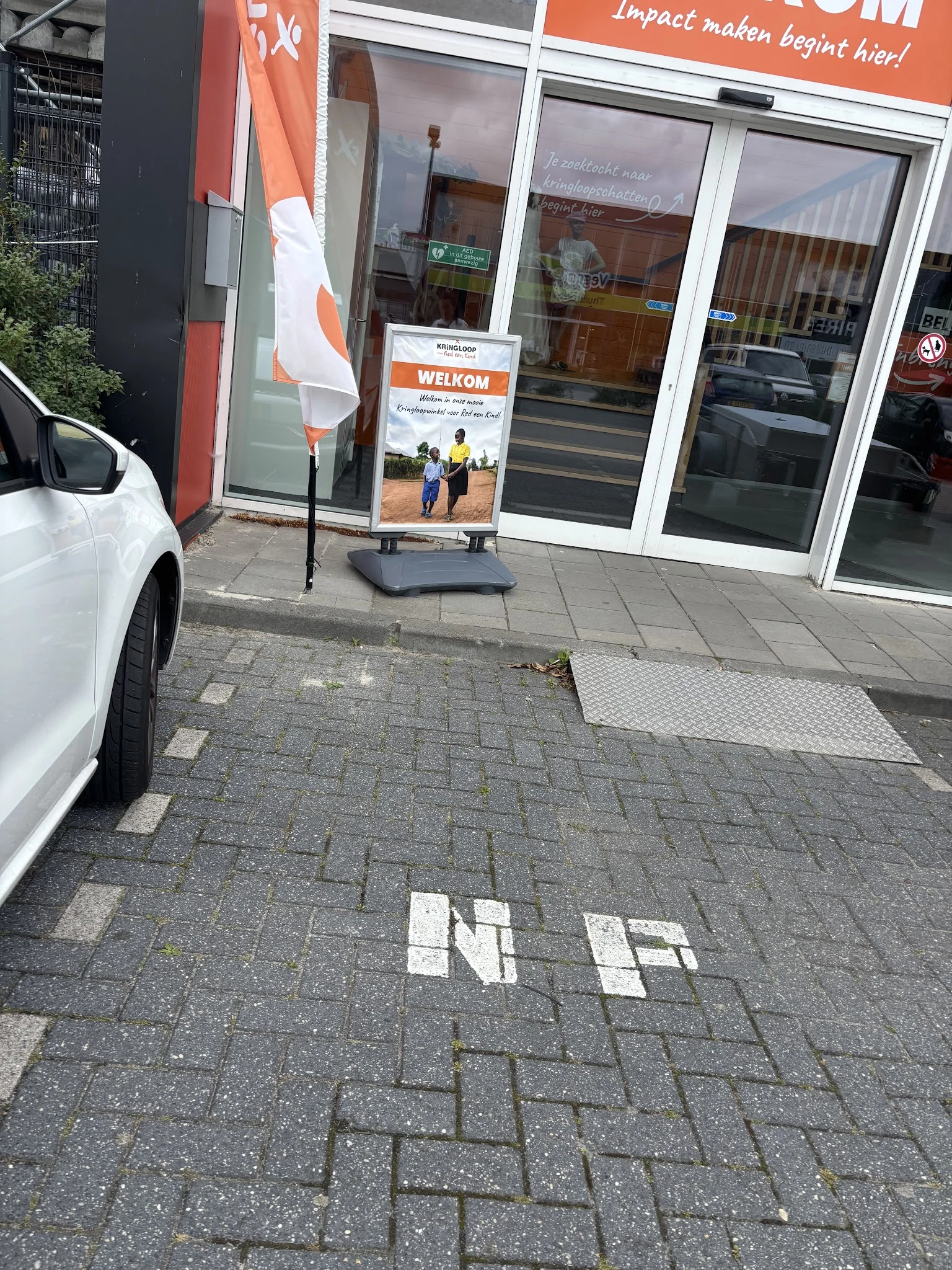 Winkelvoorgevel met witte deuren en welkomstbord, parkeerplek met witte auto linksvoor