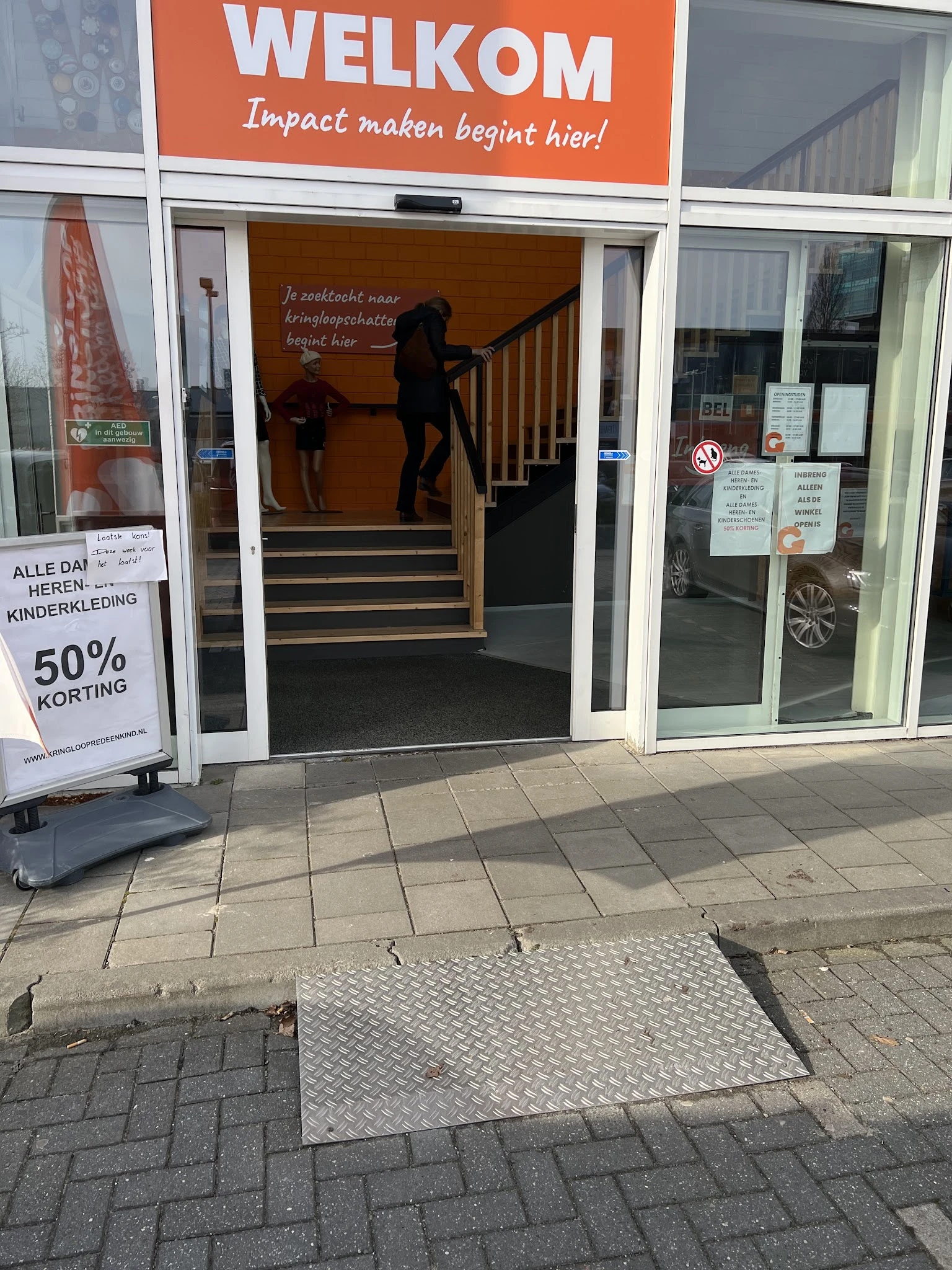 Winkelgevel met glazen deuren, trappen naar ingang, promobord met '50% korting', en personen in de ingang